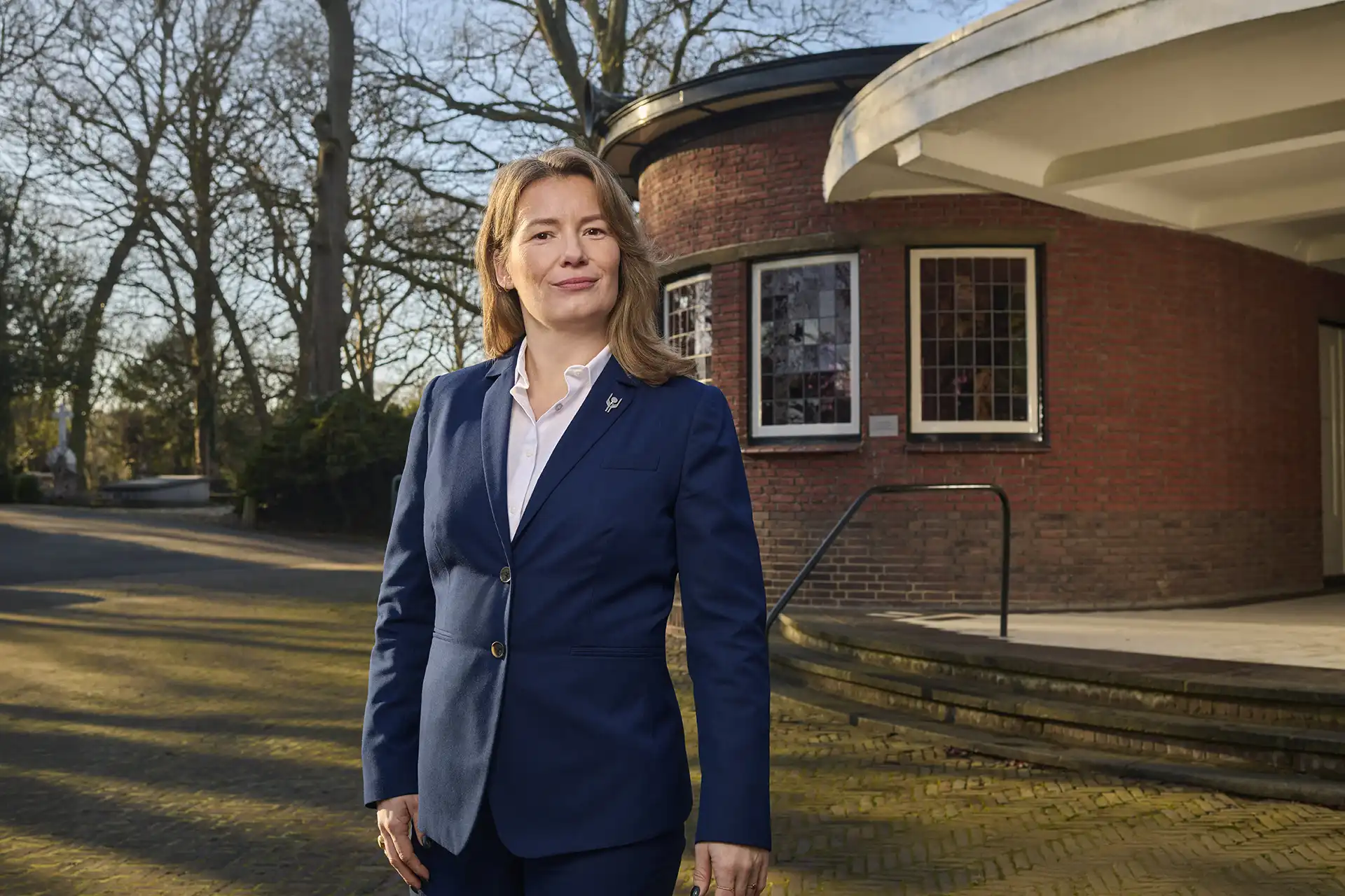 Portretfoto vrouwelijke uitvaartverzorger buiten uitvaartcentrum kijkend in camera