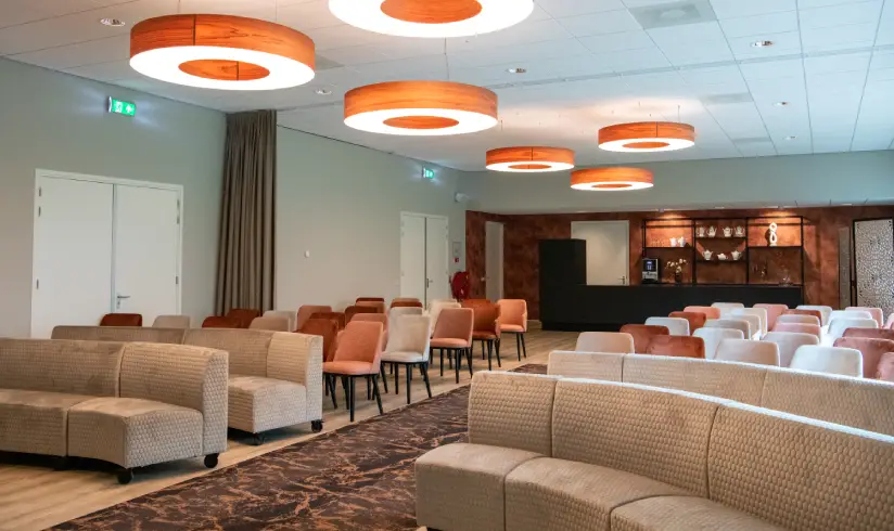 Grote zaal met 2 grote grijze banken en rijen stoelen