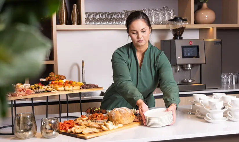 Een medewerker zet een stapel borden bij de hapjes neer.
