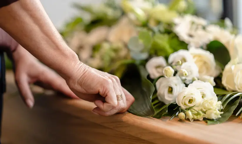 Een kist met bloemen en de handen van de nabestaande.