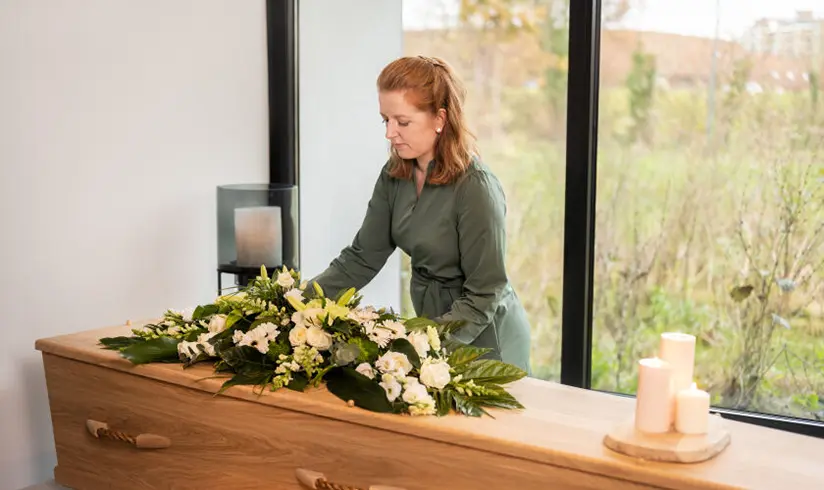 Een uitvaartverzorger staat naast een kist met bloemen