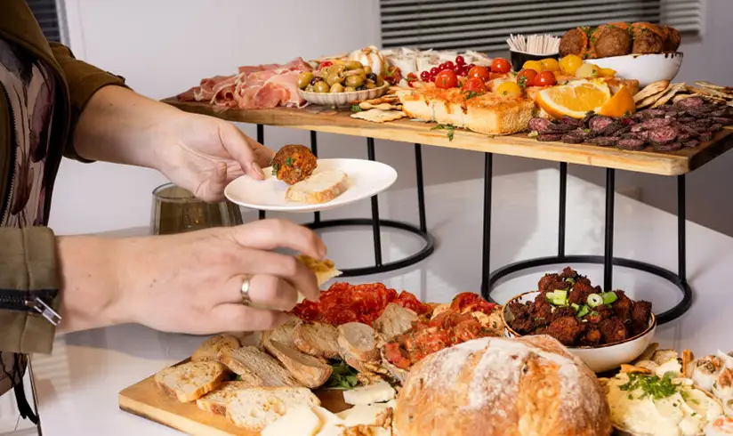 Tafel met planken vol borrelhapjes en een persoon die een bordje vult