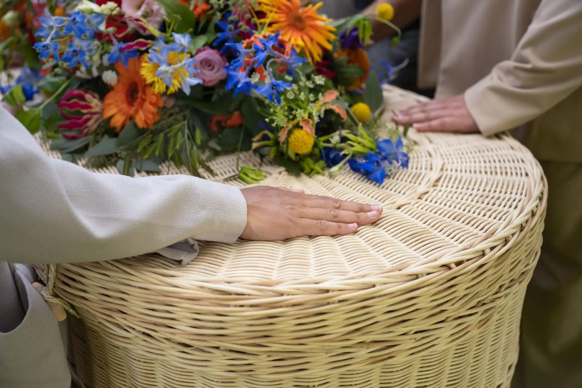 Handen op uitvaartmand met kleurrijke bloemen