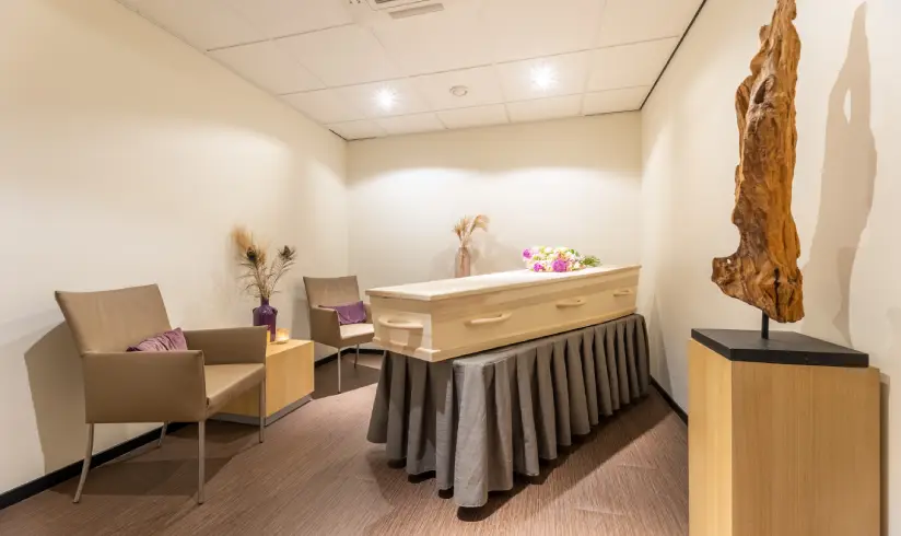 Kamer met een uitvaartkist en een stoel en standbeeld aan de muren