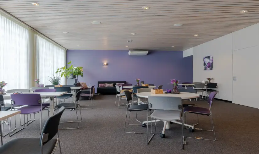 Grote ruimte met tafels en stoelen en achterin 2 zwarte banken