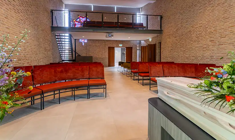 Een kapel met banken en een kruis en 2 schilderijen aan de muren