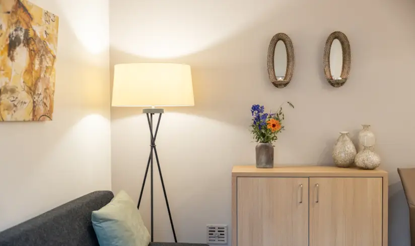 Een hoek van de kamer met een bank, lamp, en dressoir