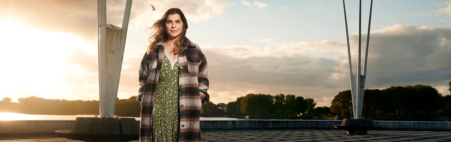 Vrouw staat op de kade kijkend in camera met zonnestralen achter haar