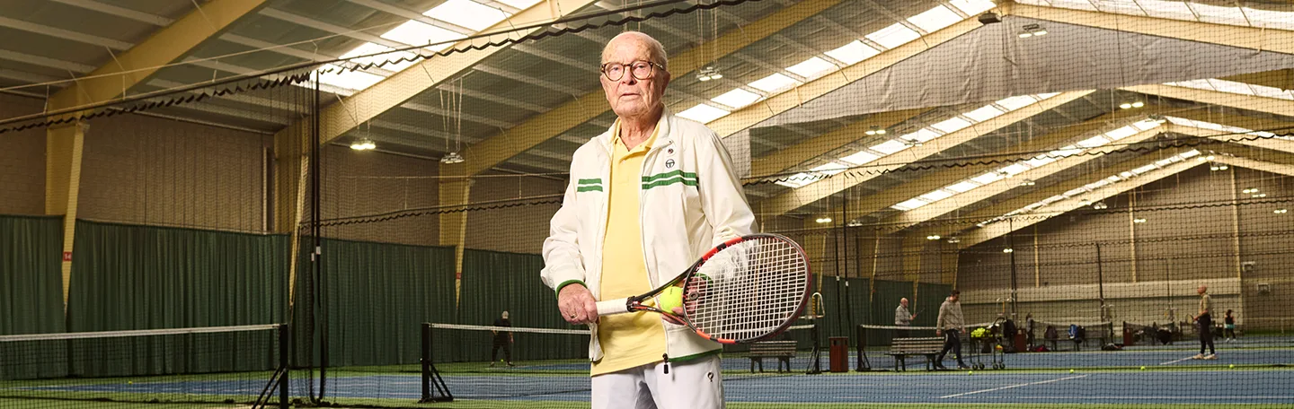 Oudere man op tennisbaan met tennisracket in handen
