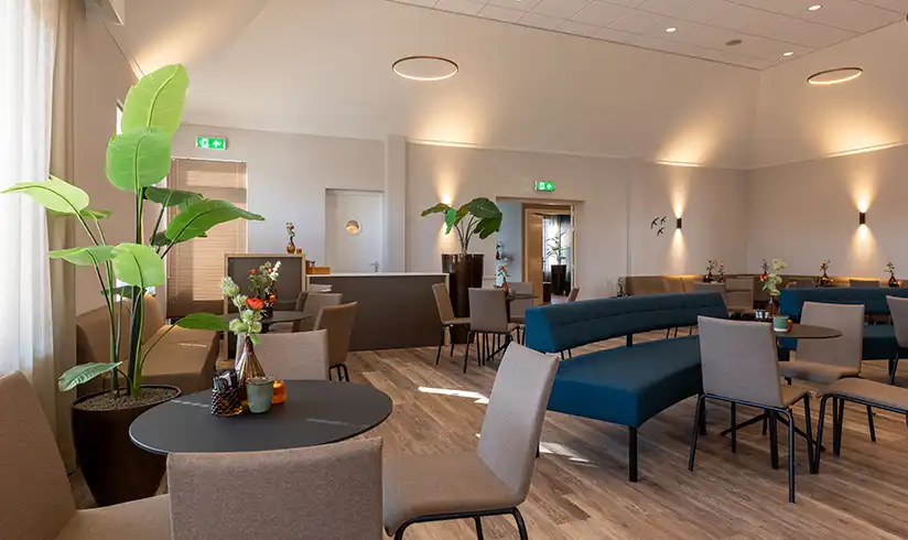 Grote ruimte met rijen stoelen en een uitvaartkist met bloemen