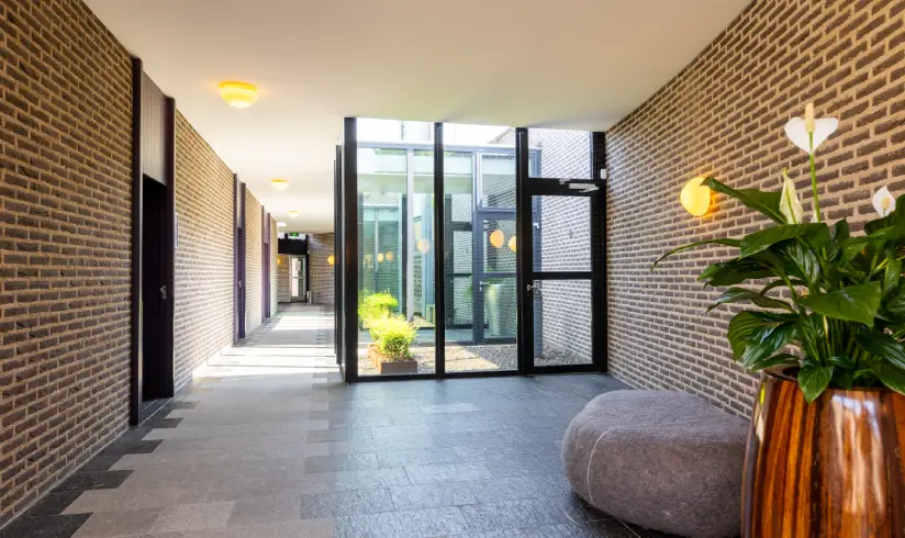 Een grote hal met meerdere patios met glazen wanden en een grote kamerplant in koperkleurige pot