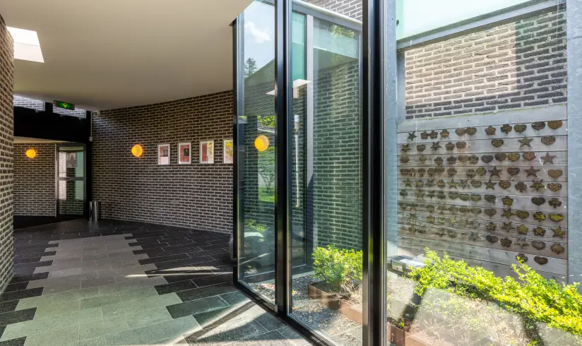Een gang met een glazen wand van waar je uitkijkt op een houten bord met hangertjes