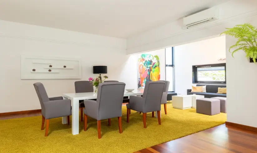 Ruimte met een geel tapijt met daarop een tafel met 6 stoelen