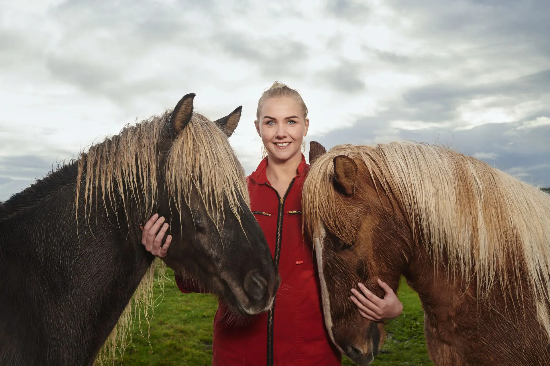 Portretfoto jonge blonde vrouw in rode overall aait twee paarden