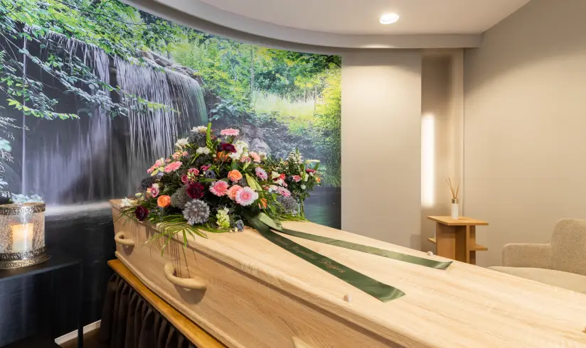 Kamer met een foto van een waterval op de muur en een uitvaartkist met bloemen ervoor