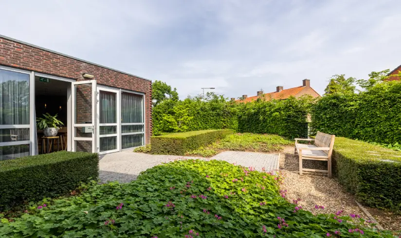 Een tuin met een bankje en groene struiken