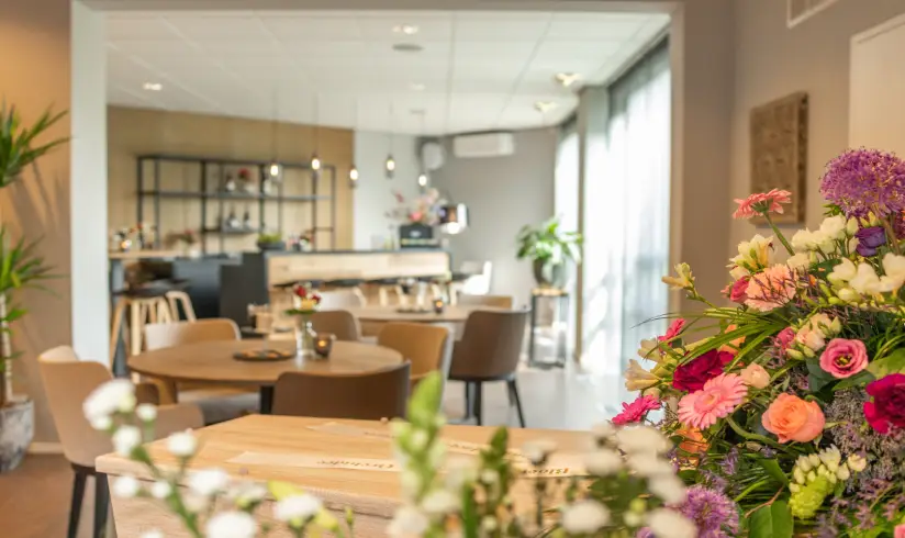Grote ruimte met bloemen op de voorgrond en veel tafels en stoelen
