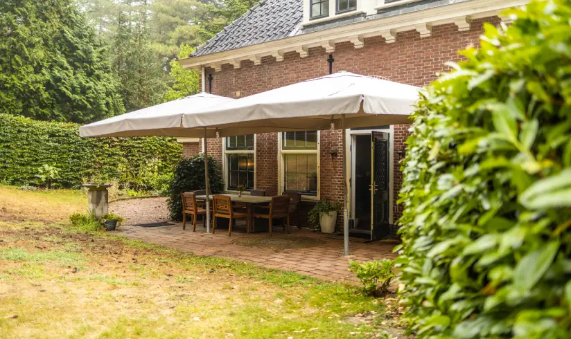 De tuin van een stenen gebouw met 2 parasols en een tafel met stoelen.