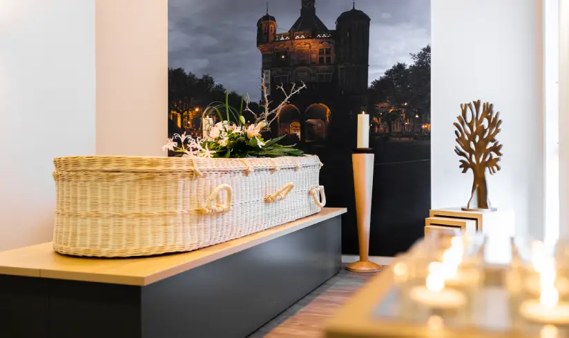 Kamer met een rieten uitvaartkist met bloemen en brandende waxinelichtjes