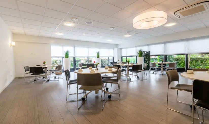 Grote zaal met tafels en stoelen en grote raampartijen