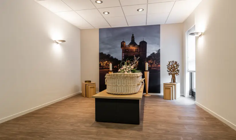 Kamer met een rieten uitvaartkist met bloemen en een schilderij aan de muur