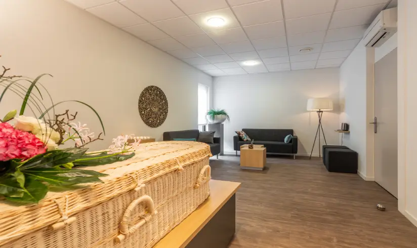 Kamer met een rieten uitvaartkist met bloemen en een zithoek