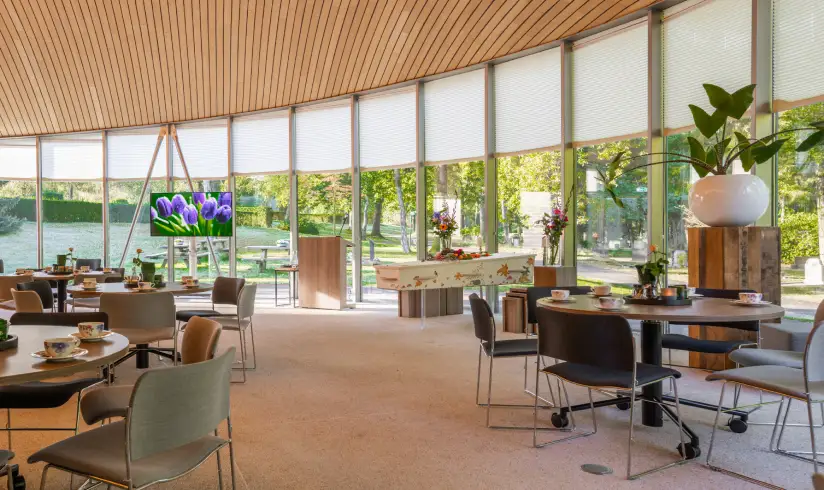 Grote zaal met tafels en stoelen en een uitvaartkist naast de ramen