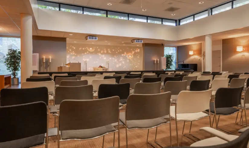 Grote zaal met meerdere rijen stoelen en een podium voorin