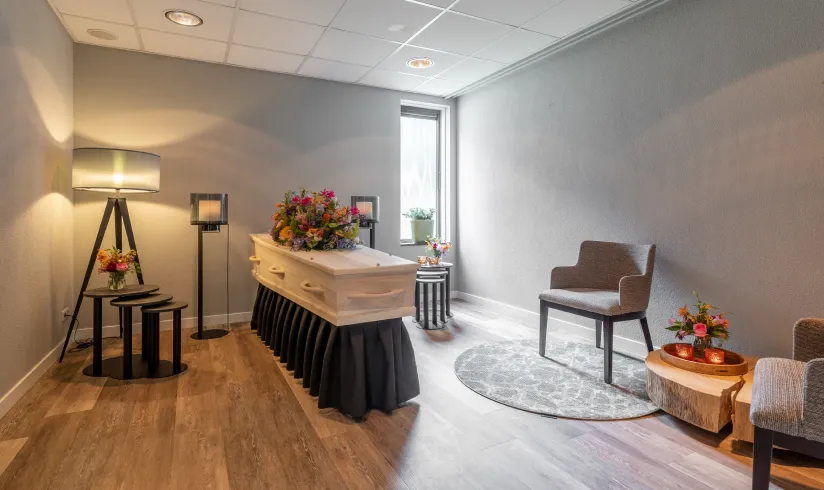 Kamer met een uitvaartkist met bloemen en 2 stoelen