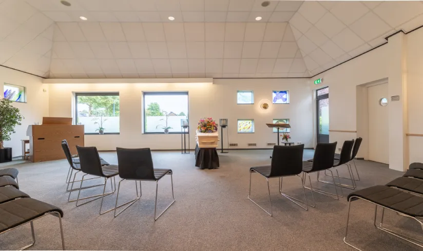 Grote ruimte met rijen stoelen een een uitvaartkist in het midden