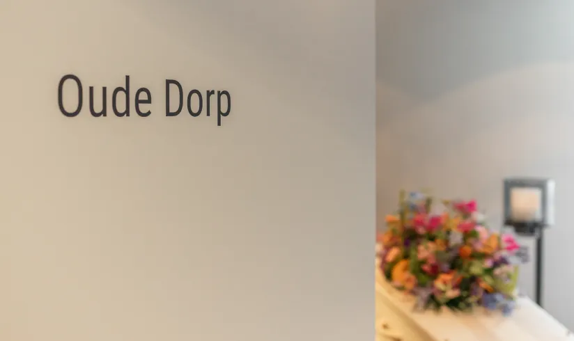 Close up van een deur waarop 'oude dorp' staat en een kist met bloemen in de achtergrond