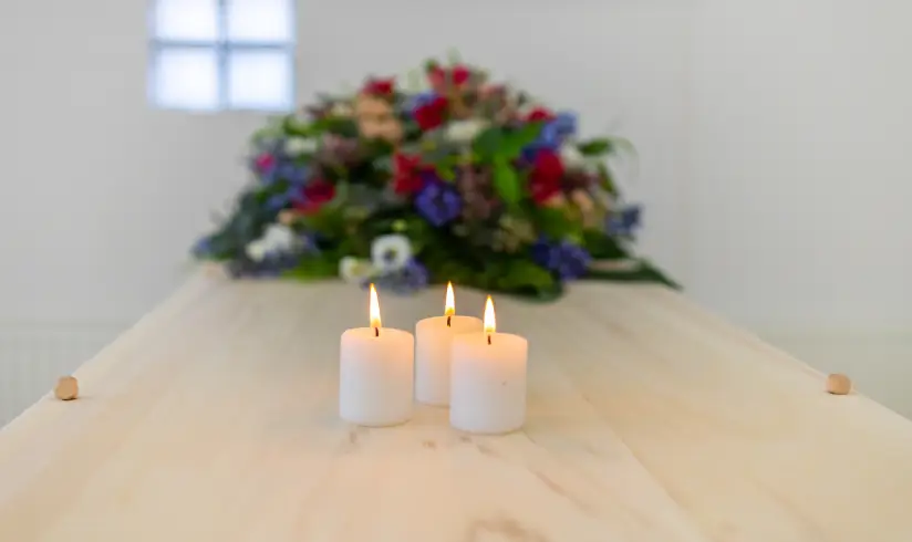 Close up van een houten uitvaartkist met bloemen en brandende kaarsjes