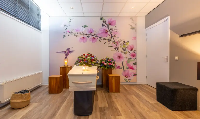 Kamer met een uitvaartkist met bloemen en een roze muurschildering