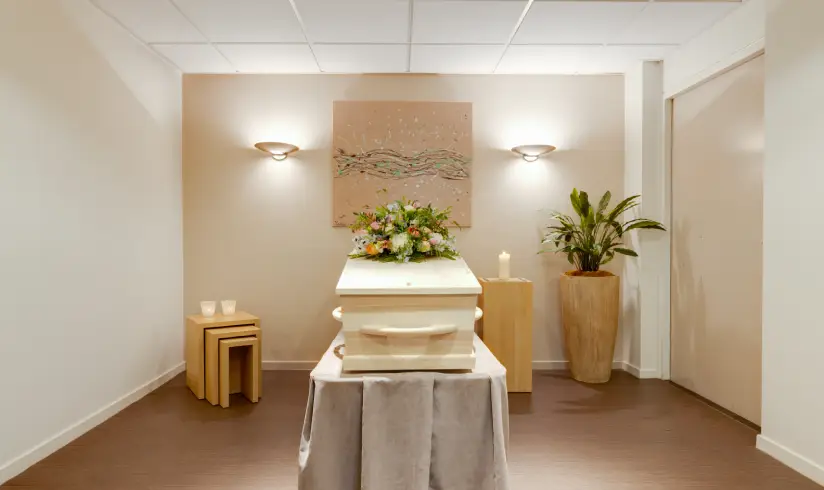 Een kamer met een houten uitvaartkist met bloemen.