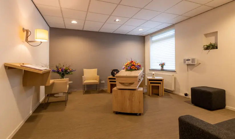 Kamer met een aantal stoelen en een kist met bloemen in het midden.