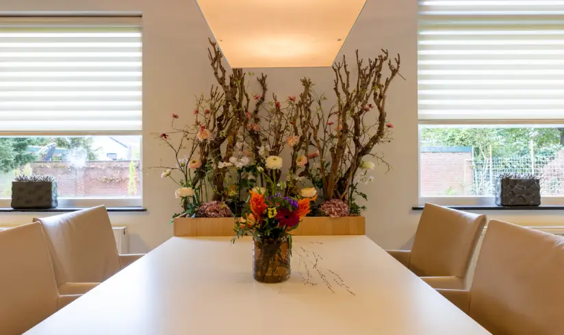 Een tafel met 4 stoelen ernaast en decoratie met takken aan de muur.