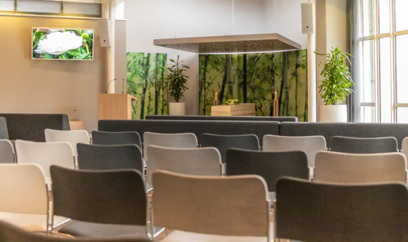 ruimte met meerdere rijen stoelen en vooraan de uitvaarkist met spreekgestoelte