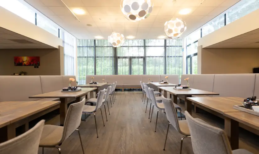 Grote ruimte met tafels en stoelen en witte, ronde hanglampen