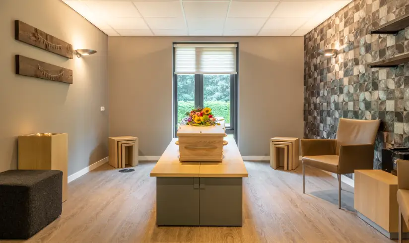 Ruimte met uitvaartkist en 2 stoelen aan de rechter muur
