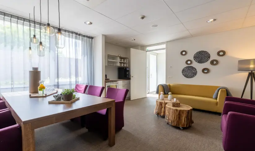 Kamer met een tafel met paarse stoelen, een gele bank en een paarse fauteuil