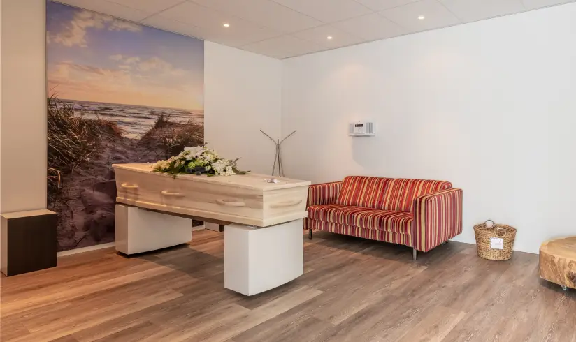 Kamer met een houten uitvaartkist met bloemen en een gestreepte bank