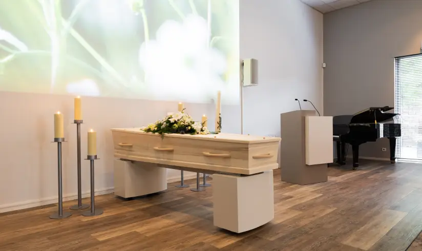 Ruimte met een houten uitvaartkist in het midden met 3 grote kaarsen en een spreekgestoelte