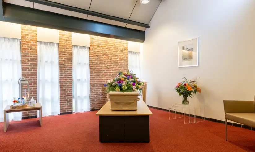 Opbaarkamer met kist met bloemen en een stoel