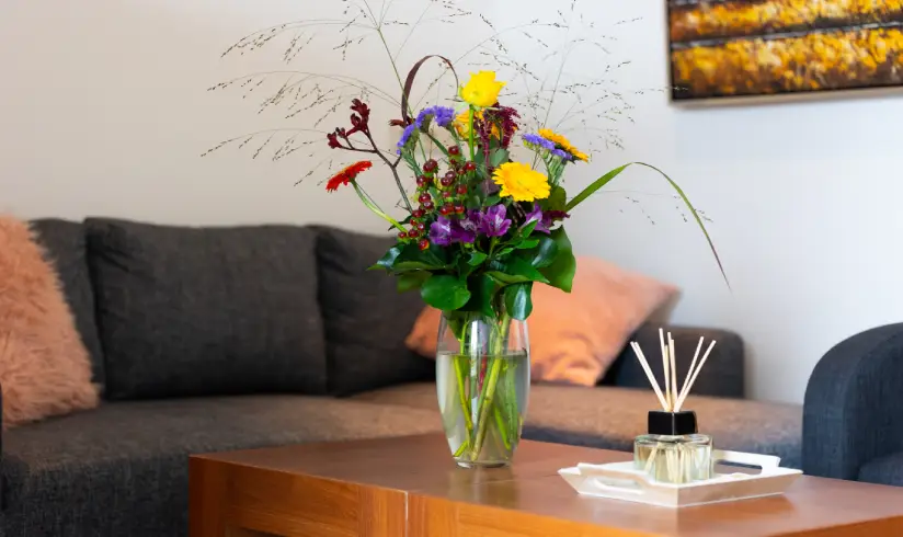 Close up van een salontafel met een bos bloemen, en een donkere bank.