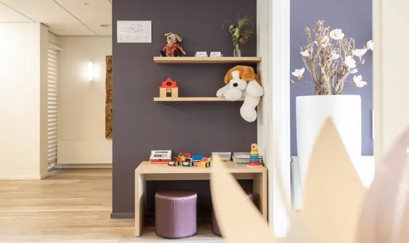 Een hoek met een paarse muur met daarvoor een tafel en 2 plankjes met speelgoed