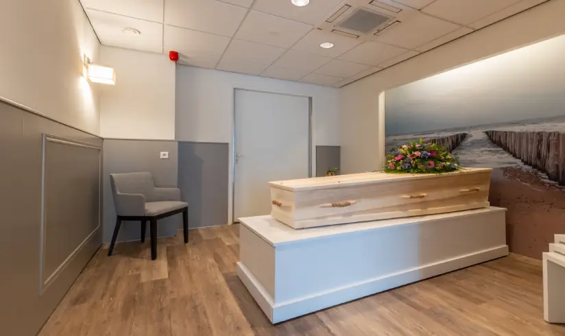 Een houten uitvaartkist met bloemen in een kamer