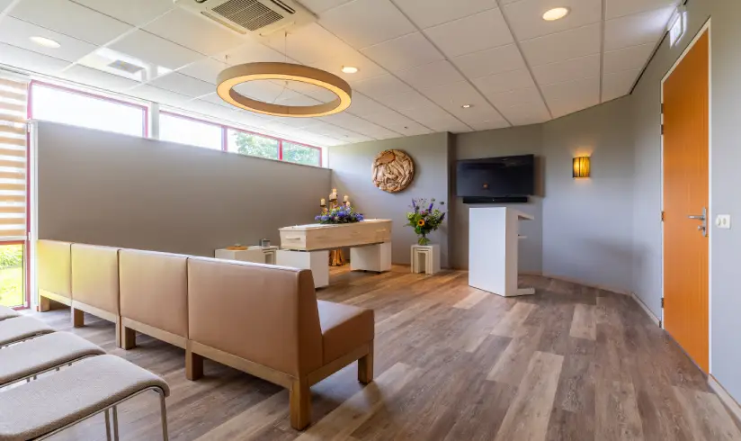 Kamer met een uitvaartkist en rijen banken en stoelen