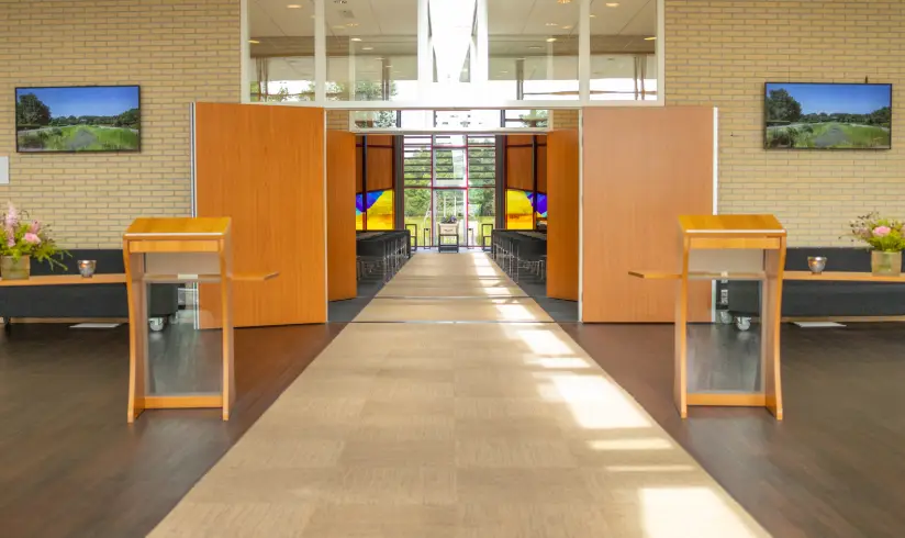 2 spreekgestoeltes in de hal met opstaande deuren naar een grote zaal met een uitvaartkist