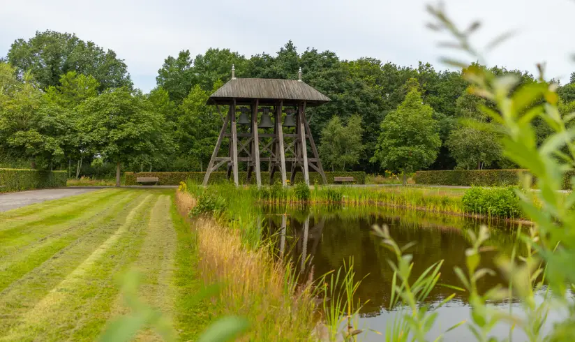 Grote vijver met gras eromheen en een grote houten constructie op de achtergrond