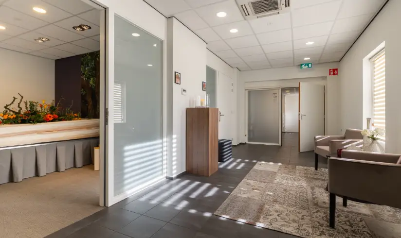 Ruimte met stoelen en aangesloten een kamer met een uitvaartkist met bloemen